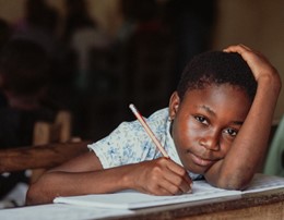 Child seated at a desk with pencil poised over paper