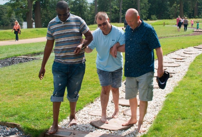 Two men walking a third man along a sensory path